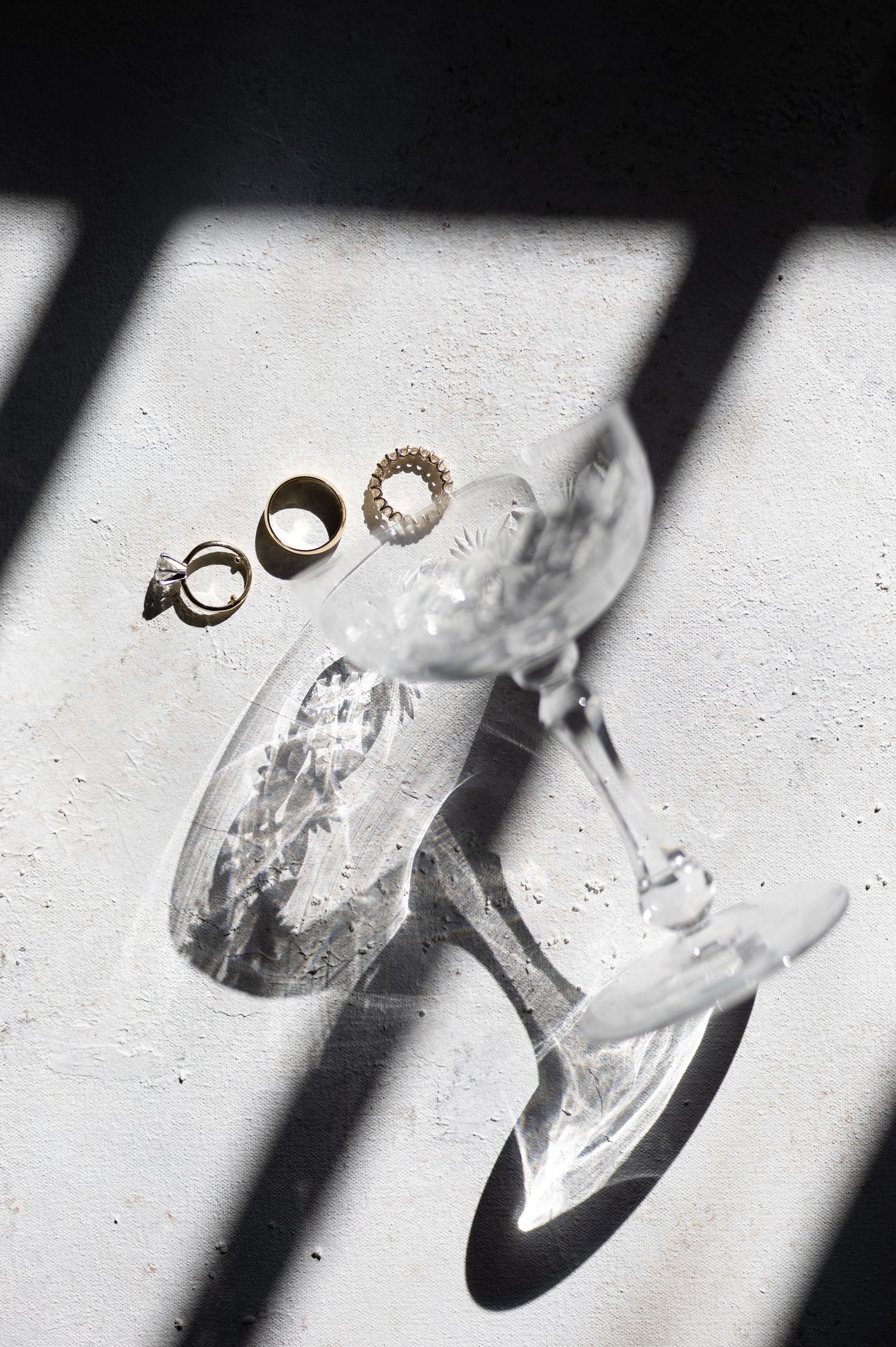 Three elegant rings displayed on a tilted champagne glass casting dramatic shadows on a light surface.