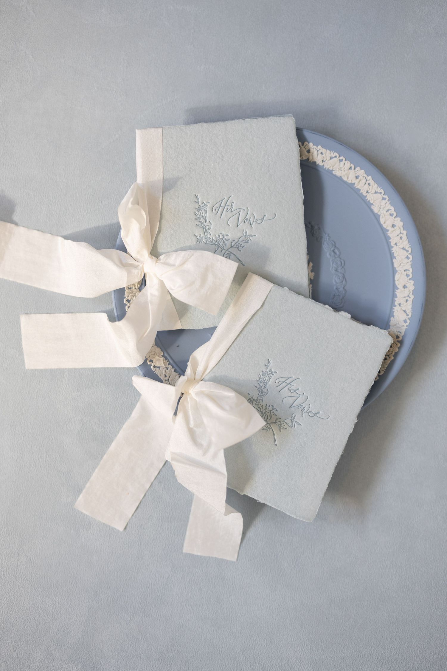 Two elegant light gray journals or notebooks with white silk ribbons tied in bows against a soft gray background.
