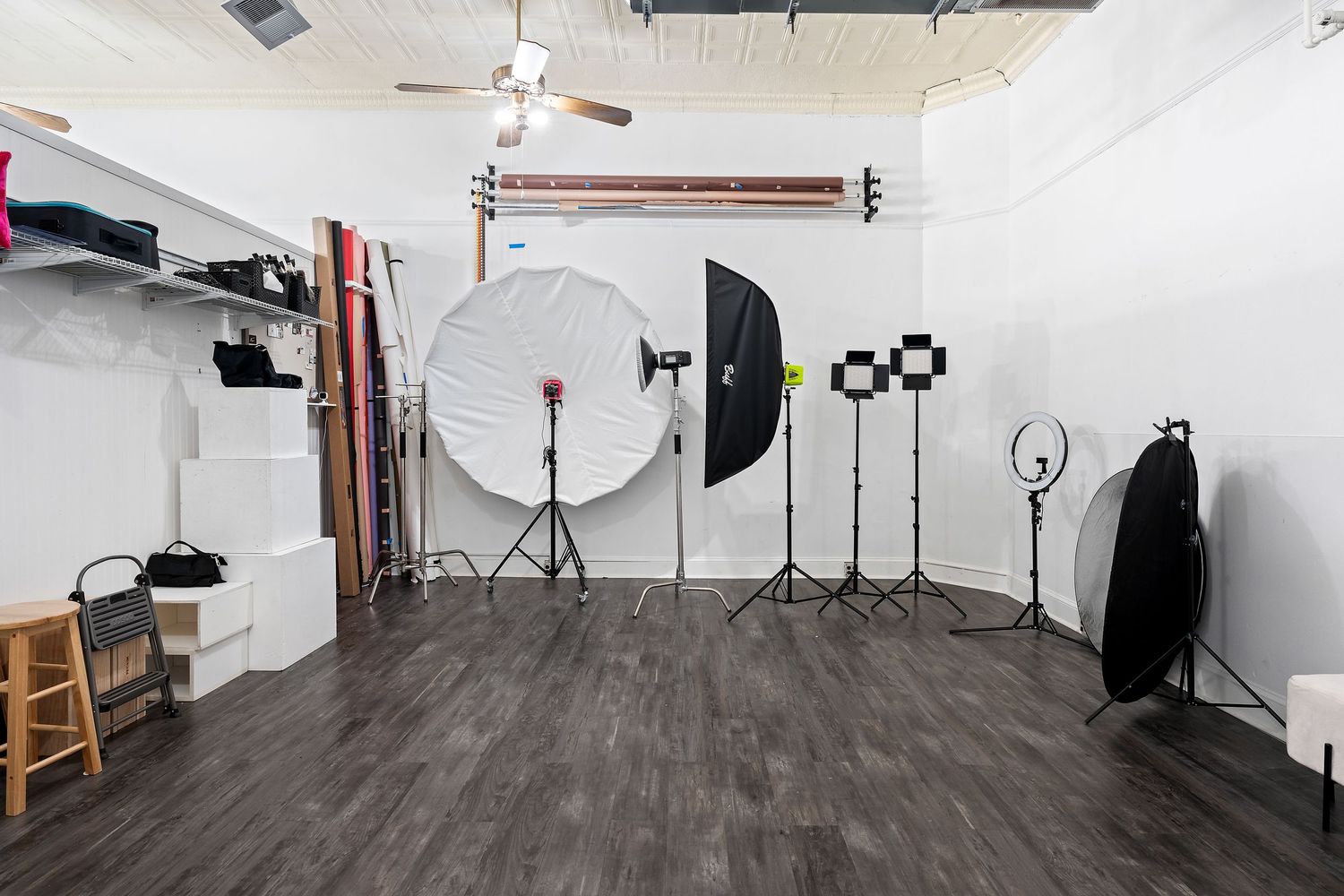 Photography studio interior with lighting equipment, white walls, reflectors and dark wooden flooring.
