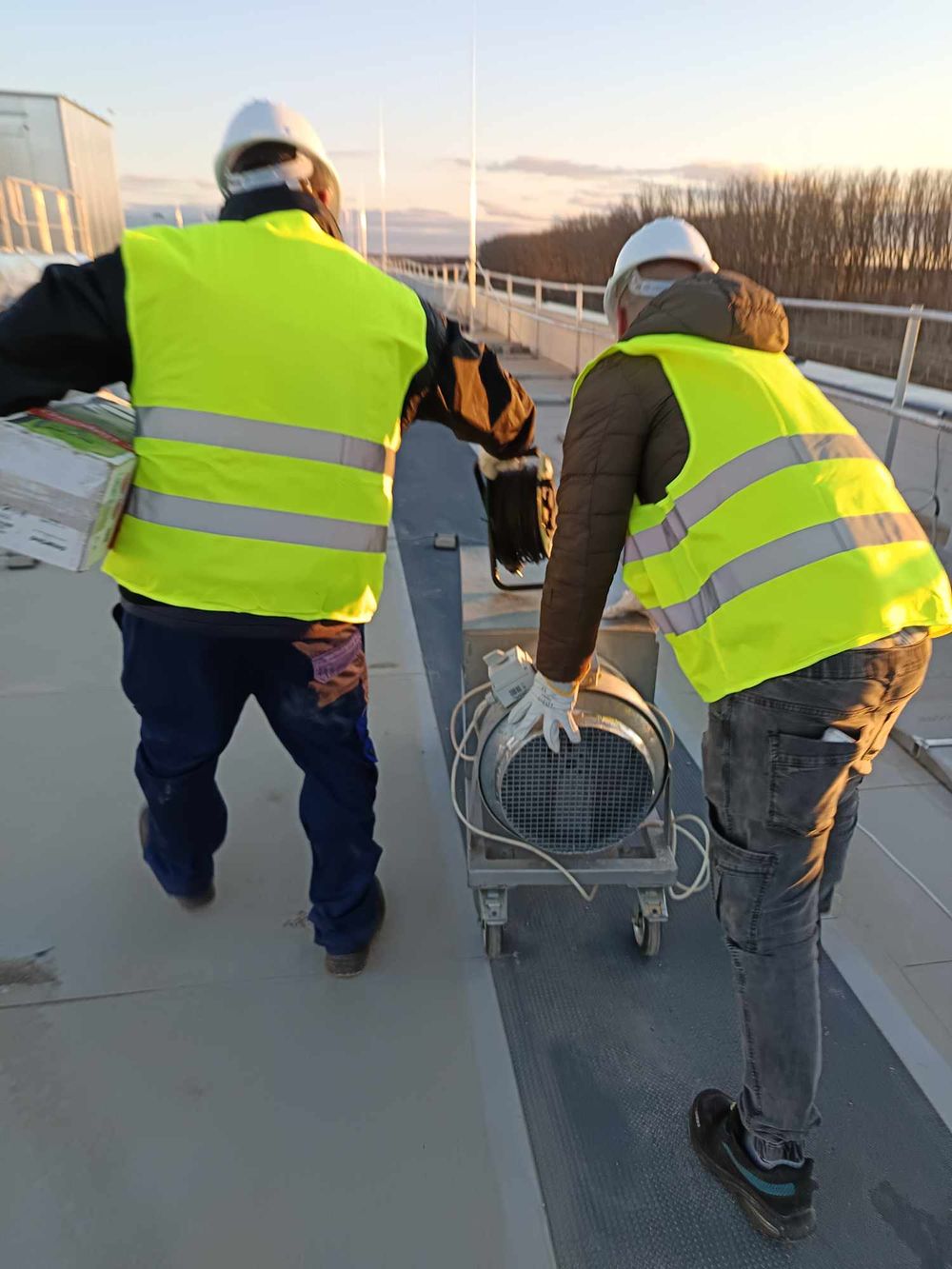 Workers in safety vests performing maintenance on rooftop equipment.