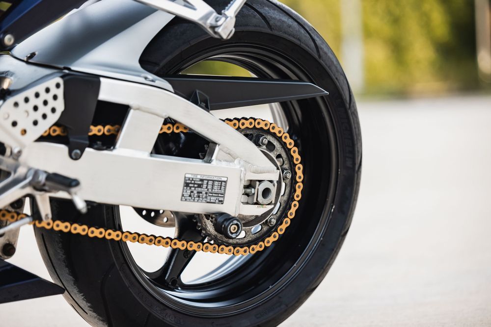 Close-up view of a motorcycle rear wheel with gold chain and white swing arm suspension.