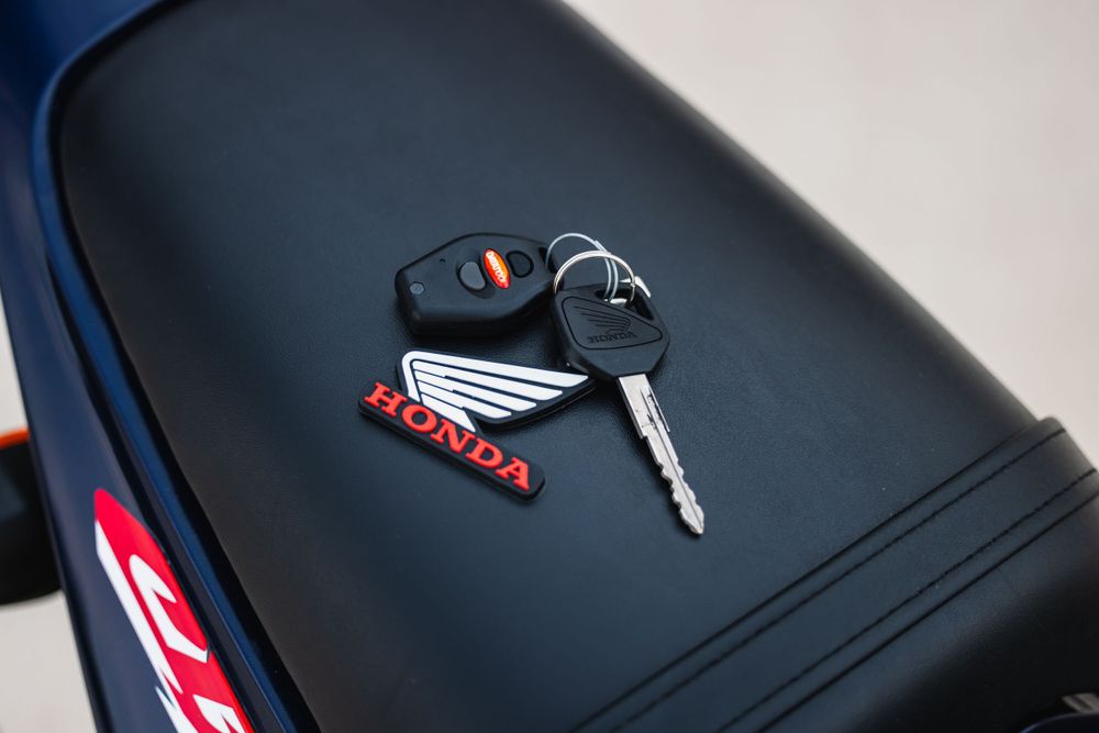 Honda motorcycle ignition key and keyring resting on black seat leather with red accent stitching.
