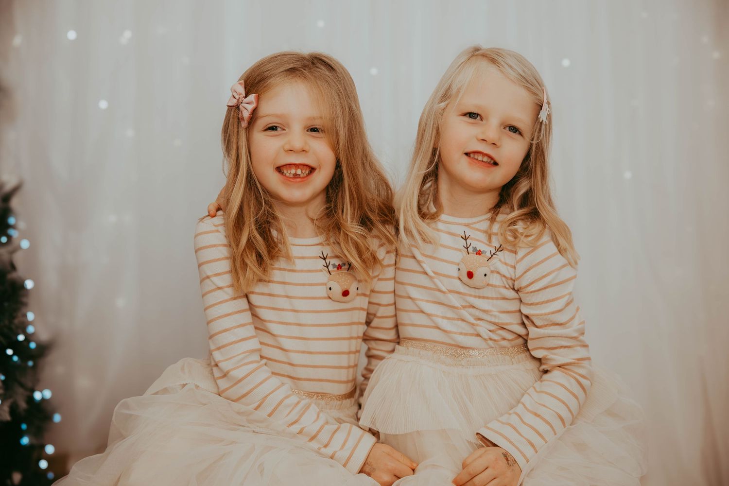 Two children in striped tops pose for holiday portrait with Christmas backdrop.