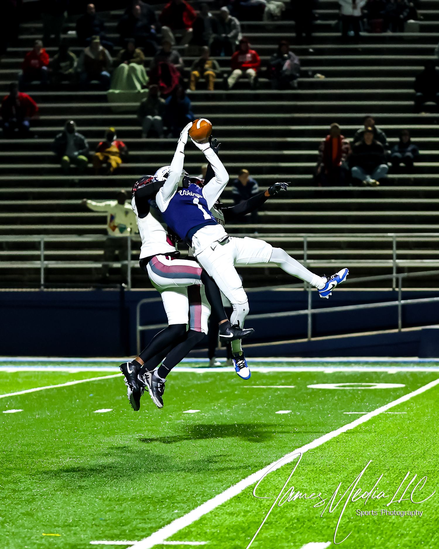 Two football players leap high into the air to battle for possession of the ball during a nighttime game.
