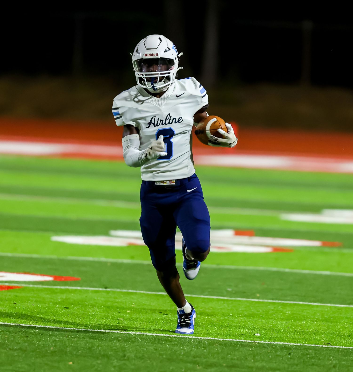 Football player in white and blue Boston uniform runs with ball down the field during nighttime game.