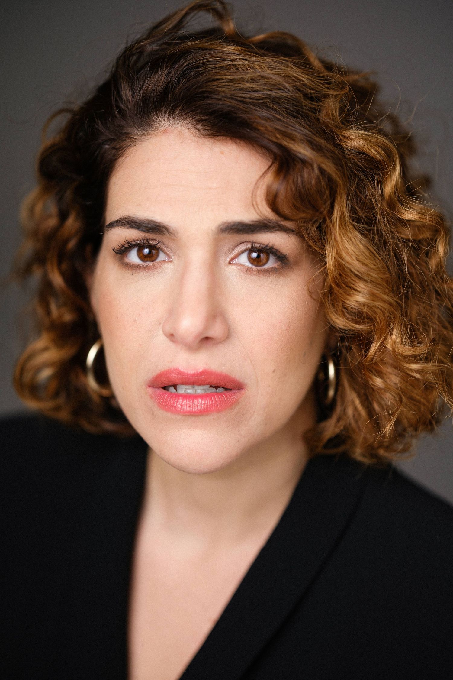Close-up portrait against dark background wearing black blazer and bright lipstick.