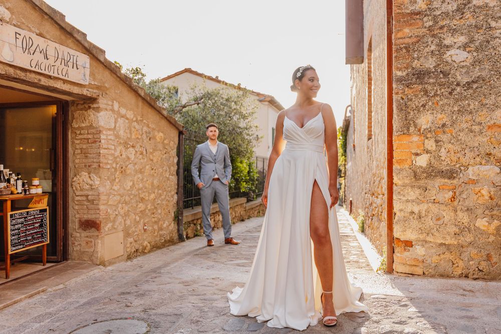 Eine Braut in einem fließenden weißen Kleid geht durch charmante gepflasterte Straßen. Monteriggiano Toskana Italien