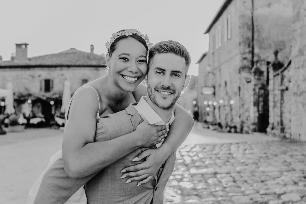 Ein fröhlicher Huckepack-Moment, der in Schwarzweiß vor historischer Architektur festgehalten wurde. Monteriggiano Toskana Italien