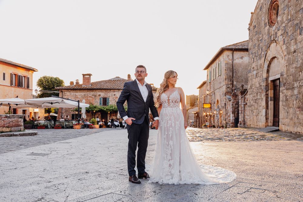 Ein romantisches Hochzeitspaar posiert bei Sonnenuntergang auf einem charmanten italienischen Dorfplatz. Monteriggiano Toskana Italien