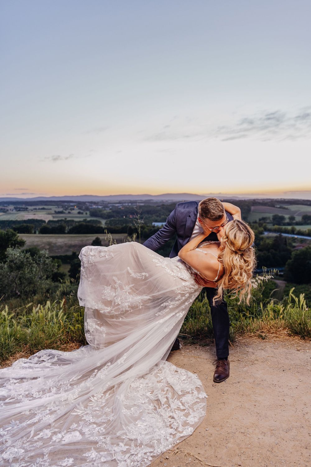 Ein dramatisches Hochzeitsfoto bei Sonnenuntergang auf einem Hügel, das ein geschwungenes Spitzenkleid zeigt. Monteriggiano Toskana Italien