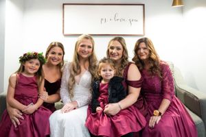 Wedding party seated on couch wearing burgundy dresses and floral crowns.