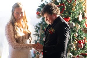 Winter wedding ceremony moment with decorated Christmas tree in background.