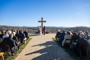 Outdoor mountain wedding ceremony setup with wooden cross and rows of chairs.