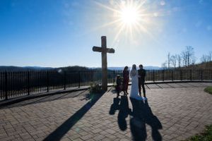 Silhouetted wedding ceremony against mountain backdrop with cross and sunburst.
