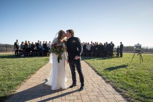 Newlyweds share a kiss on a stone path with wedding guests in the background.