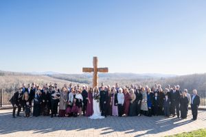 Large wedding group photo of guests gathered around a wooden cross on a hilltop.