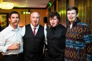 Group of men in formal attire smiling at evening reception.