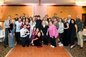Large group of people gathered in a formal event venue with chandelier lighting and white backdrop.
