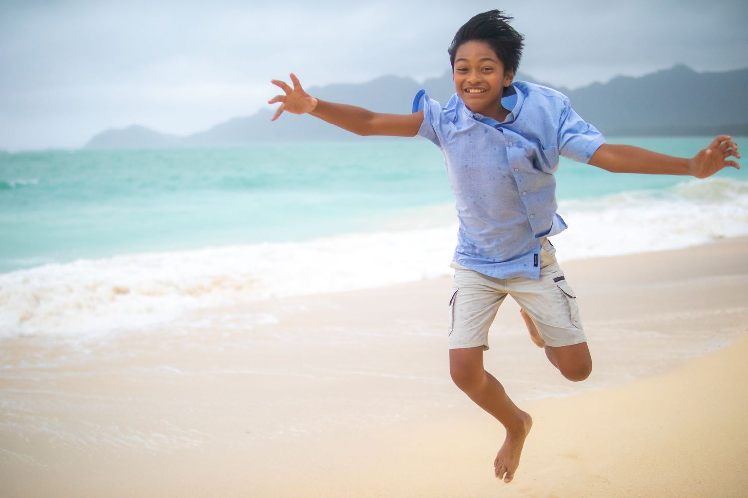 Young boy jumping toward the camera with ocean behind him — fun, energetic Hawaii beach photo by Live Tribe Media.