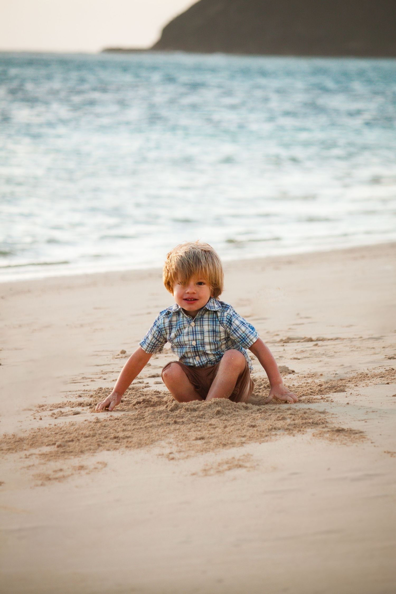 Young boy sitting on the sand at the beach — simple, candid Hawaii childhood moment by Live Tribe Media.