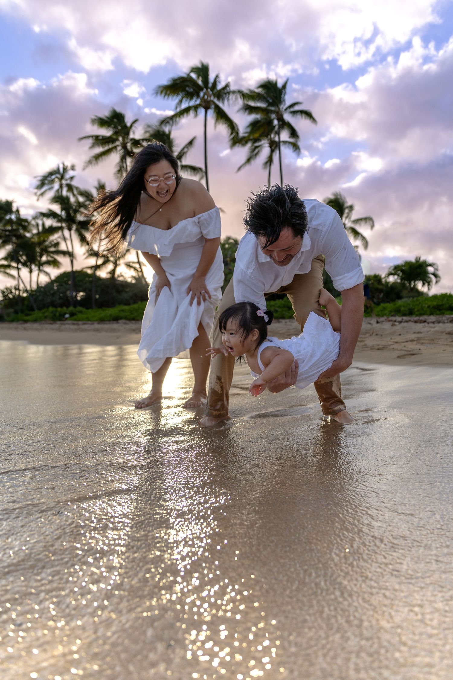 Dad holding baby over the ocean as mom watches — emotional Hawaii family moment by Live Tribe Media.