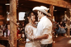 Couple shares first dance under warm string lights in rustic barn venue.