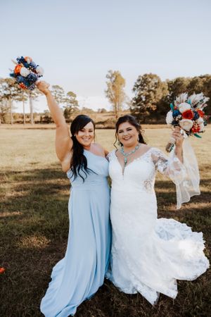 Wedding party celebrates in a sunny field with blue bridesmaid dresses and floral bouquets.