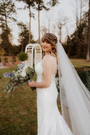 Classic bridal portrait featuring a flowing veil and blue and white bouquet in an outdoor garden setting.