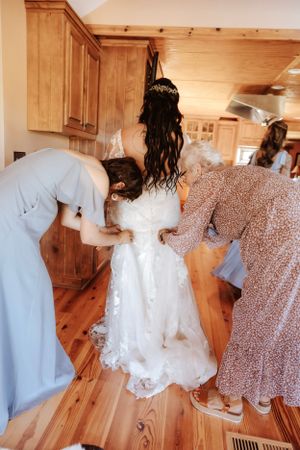 Wedding party members in blue dresses and white gowns prepare together on hardwood floors.