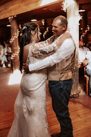 Wedding couple dances together in rustic barn venue decorated with string lights.
