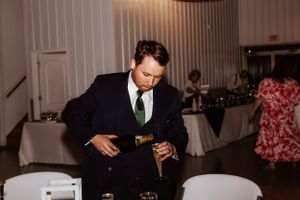 Wedding guest in formal attire pours champagne at an indoor reception.