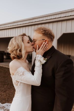 A romantic wedding portrait of a couple sharing a tender kiss outdoors in warm lighting.
