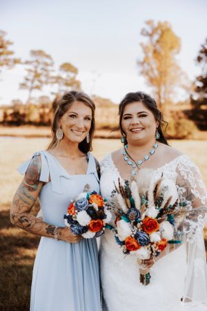 Wedding party members hold vibrant red and blue bouquets while posing in golden afternoon light.