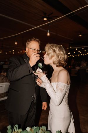 A couple sharing wedding cake during their reception under string lights.