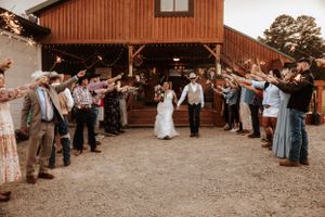 Wedding guests form an aisle outside a rustic barn venue for the newlyweds' grand exit.