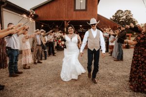 Wedding couple exits their barn venue celebration while guests throw confetti in celebration.