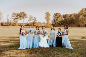 Bridesmaids in light blue dresses pose together in golden sunset light.