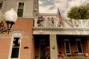 Row of historic brick buildings with American flags and classic lampposts along a small town street.