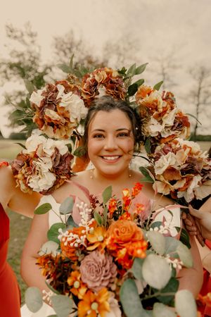 Autumn wedding bouquet featuring orange and burgundy flowers with eucalyptus leaves in rustic outdoor setting.
