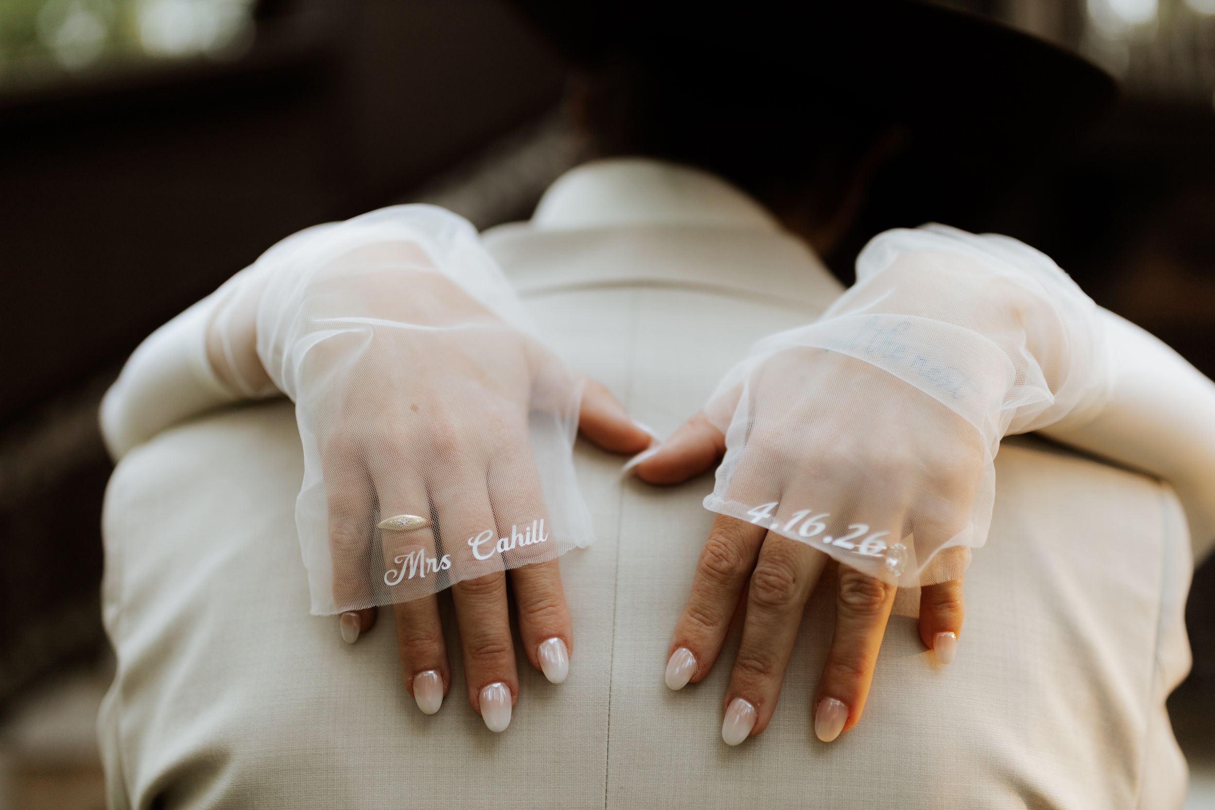 Bride wearing sheer gloves with Mrs. and Mr. written on fingers, hands resting on groom's back.
