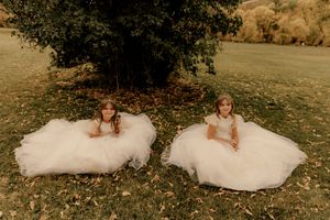 Wedding party members in formal attire pose on grass with fall foliage in the background.