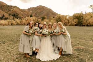 Bridal party in sage green dresses poses against mountain backdrop during fall wedding.