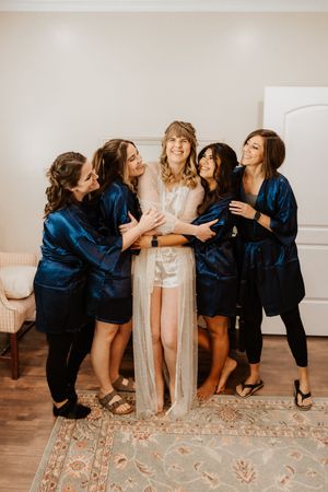Wedding party in blue robes poses playfully on decorative rug during getting ready photos.