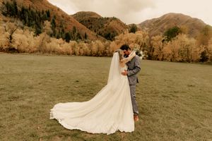 Wedding couple embraces in a scenic mountain meadow with dramatic peaks in the background.