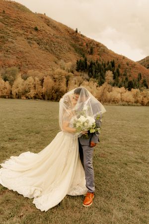 A couple shares an intimate moment under a veil against a backdrop of autumn mountains and trees.