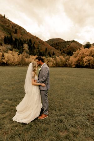 Newlyweds embrace in a scenic mountain valley with golden autumn trees in the background.
