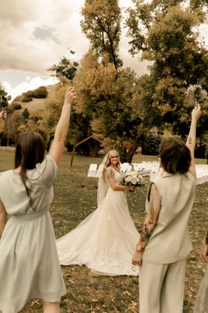 Bridesmaids in sage dresses celebrate with the bride during an outdoor autumn wedding.