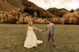 A bride and groom pose playfully in a mountain meadow surrounded by fall foliage.