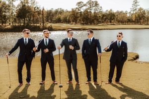 Groomsmen lined up along waterfront for casual wedding party photo.