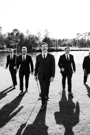 Black and white photo of groomsmen casting long shadows while walking.